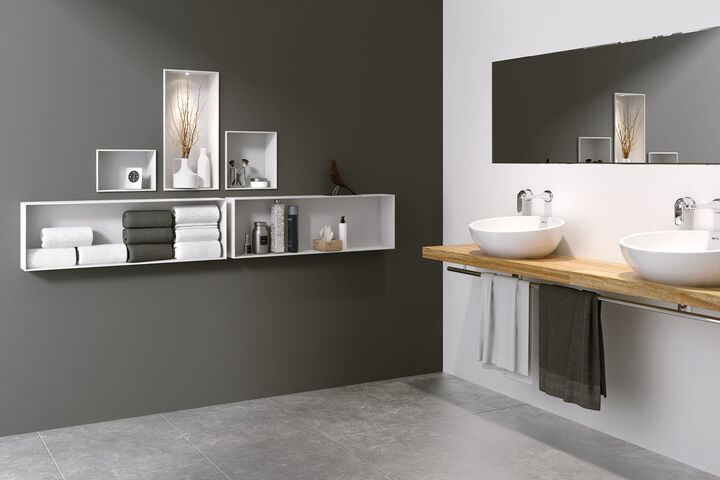 Badezimmer, auf der rechten Seite befindet sich ein hölzerner Waschtisch mit zwei Waschbecken und Spiegel darüber. Auf der Grauen Wand links sind Elemente von Duschboard Multistar Plan Plus von Schedel eingelassen. Sie fungieren als Regel für Handtücher, Designobjekte und Hygieneartikel.
